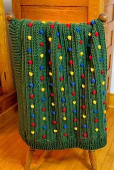 a green blanket with multicolored buttons on it sitting on a wooden stand in front of a chair