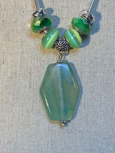 "This New Dione necklace comes with one large Striped Agate pendant, 2 Green Cats Eye Dione glass beads with silver tone grommets, 2 Green and White Crystal Dione beads with silver tone grommets and two silver tone bead stoppers to keep it all in place.  You have the choice of a 16\", 18\" or 24\" silver plated brass snake chain necklace with lobster clasp. The Pendant Measures: 1 1/2\" X 1\" The Beauty of this Dione add a bead system is that you can buy new colors of bead sets to put on your necklace to match your outfit or mood.  The end of the necklace screws off to change to the color of beads you want. (New Jewelry NA266 & 267) We also have vintage jewelry, Christmas ornaments, Vintage glassware and many other items.  We will combine shipping for multiple items if possible!" Silver Jade Beaded Necklaces As Gift, Silver Necklaces With Large Czech Glass Beads, Silver Jade Beaded Necklace As Gift, Silver Necklace With Large Czech Glass Beads, Silver Glass Jewelry With Large Beads, Silver Agate Jewelry With Large Beads, Jade Beaded Necklaces With Large Beads For Gifts, Silver Gemstone Beads Necklace With Glass Material, Silver Glass Necklace With Gemstone Beads