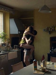 two people hugging each other in a kitchen with yellow walls and flooring on either side of the table