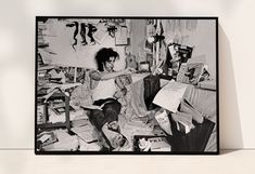 a black and white photo of a woman sitting on the floor surrounded by clutter