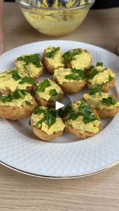 a white plate topped with mini cornbreads covered in cheese and green herbs next to a bowl of dip