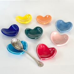 six heart shaped dishes with spoons in them on a white surface, one is empty