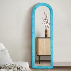 a blue mirror sitting on top of a wooden floor next to a bed and nightstand