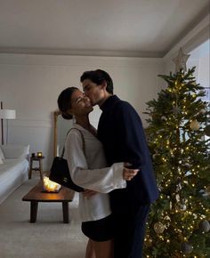 a man and woman are kissing in front of a christmas tree with lights on it