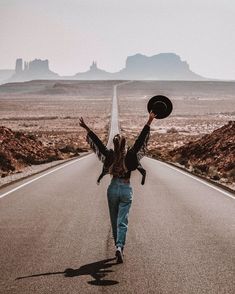 a woman is walking down the road with her arms in the air and hat raised above her head