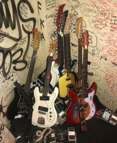 several guitars are lined up against a wall covered in graffiti