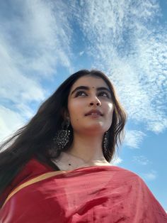 a woman with long hair wearing a red sari and earrings looking up into the sky