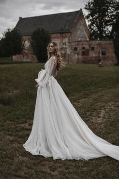 a woman in a white wedding dress standing on the grass with her back to the camera