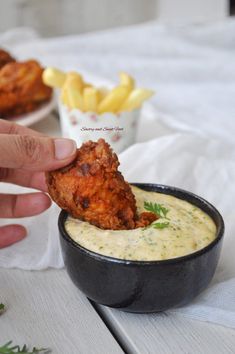 a person dipping some food into a small black bowl on top of a white table