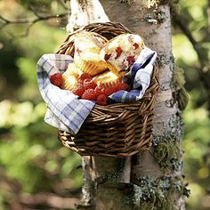 a basket filled with muffins and strawberries on top of a tree trunk