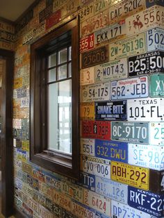 a wall with many license plates on it and a window in the middle that has a wooden frame