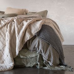 an unmade bed with several pillows and blankets on it, in a white room