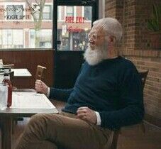 an older man sitting at a table in front of another man with a long white beard