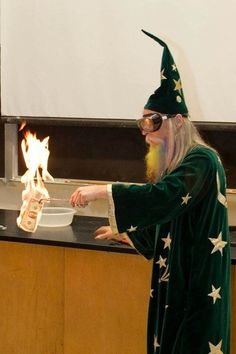 an old man dressed in green and white holding a bowl with fire coming out of it