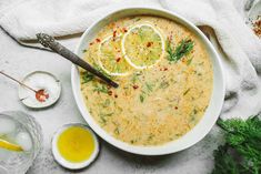 a white bowl filled with soup next to two lemons and some herbs on top