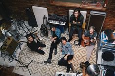 a group of young men sitting next to each other on top of a floor covered in musical equipment