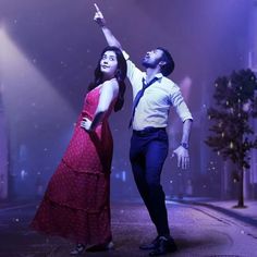 a man and woman are dancing on the street in front of bright lights at night