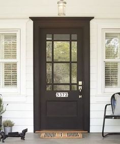 a black front door on a white house with two chairs and potted plants next to it