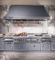 an industrial style kitchen with stainless steel appliances and marble counter tops, along with pots and pans on the hood