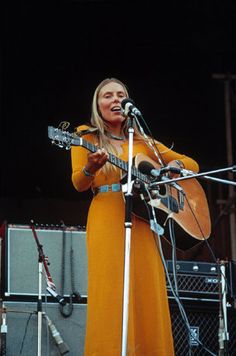 a woman standing in front of a microphone and holding a guitar on top of a stage