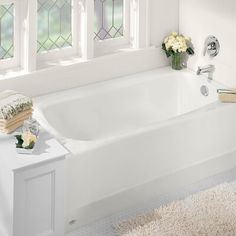 a white bath tub sitting in a bathroom next to two windows and a rug on the floor