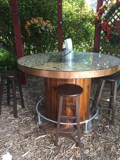 an outdoor table with two stools and a glass top in the middle of some straw