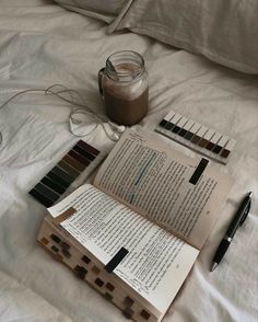 an open book sitting on top of a bed next to a cup of coffee and pen