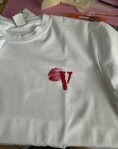 a white shirt with the letter v painted on it next to some scissors and tape