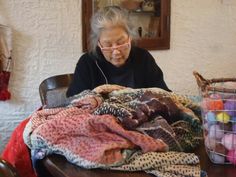 an older woman sitting at a table with many blankets and balls in front of her