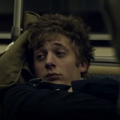 a young man sitting on a bus with his head propped up against the seat and looking off into the distance