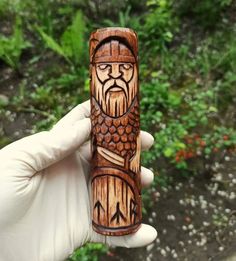 a hand holding a carved wooden object in front of green plants and trees behind it