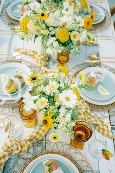 the table is set with yellow and white flowers in vases, plates and napkins