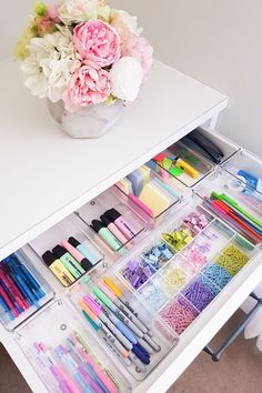 an organized drawer with pens, pencils, markers, and flowers in it on a white table