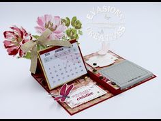 an open red box with a calendar and flowers on it's side, in front of a white background