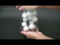 a person holding a glass filled with lots of white balls on top of a black surface