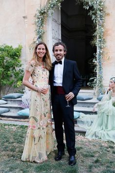 a man and woman standing next to each other in front of a building with flowers on it