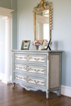 an antique dresser with flowers on top and a mirror in the corner next to it