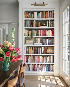 a vase with flowers on top of a table in front of a bookshelf