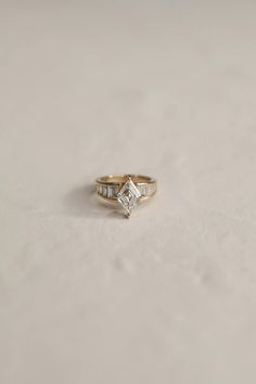 a gold ring with a princess cut diamond set in the center, on a white surface