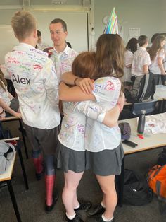 two people hugging each other in front of a class room full of students wearing birthday hats