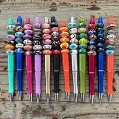 many different colored pens are lined up on a wooden surface with one pen in the middle