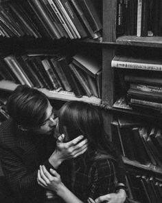 black and white photo of two people kissing in front of bookshelves with stacks of books behind them