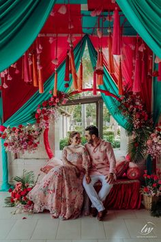 a man and woman sitting in front of a red and green stage with flowers on it