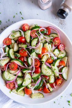 a white bowl filled with cucumber, tomatoes and onions on top of a table