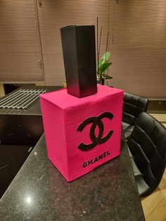 a pink chanel bottle sitting on top of a black table next to a plant