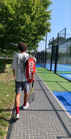 a man walking down a sidewalk with a tennis racket in his hand and a bag on his back