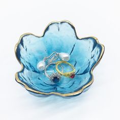 a blue flower shaped bowl with two rings in it and pearls on the bottom, sitting on a white surface