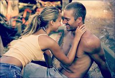 a man and woman sitting next to each other on the ground with their arms around each other