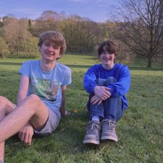 two young men sitting on the grass smiling