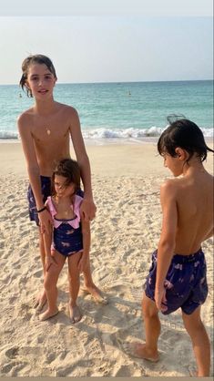 three young children standing on the beach in swimsuits